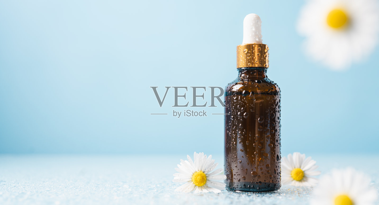 化妆瓶与吸管和水滴在柔和的蓝色背景与洋甘菊花照片摄影图片