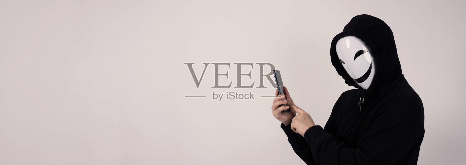 匿名黑客手持智能手机和面具，在白色背景下进行网络犯罪数据窃取照片摄影图片