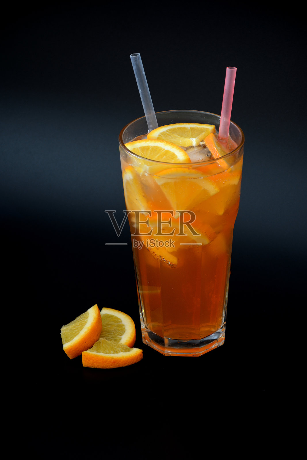 橙汁盛在高脚杯里，黑色背景上有冰块和吸管，旁边是成熟的柑橘片。照片摄影图片