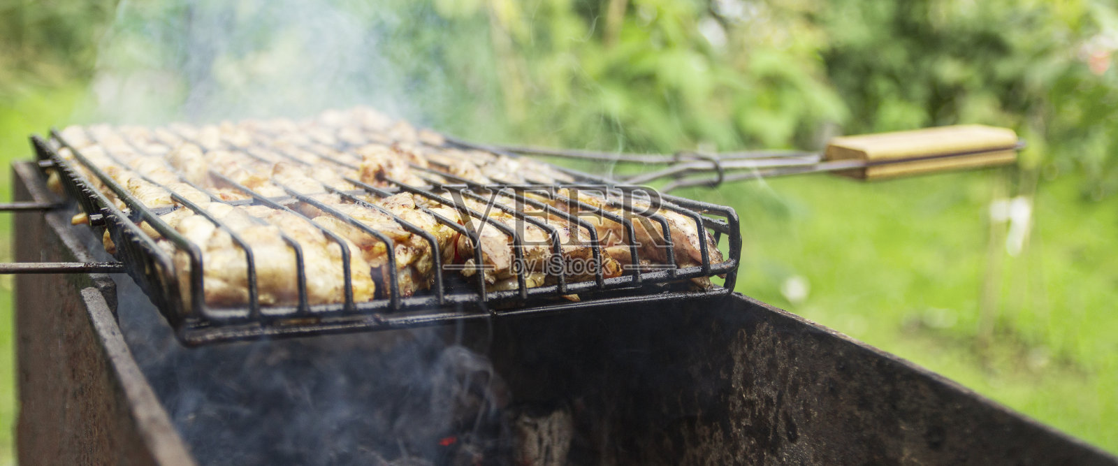 在烤架上烤鸡。在户外烧烤架上烤鸡腿，背景是火焰和烟雾。照片摄影图片
