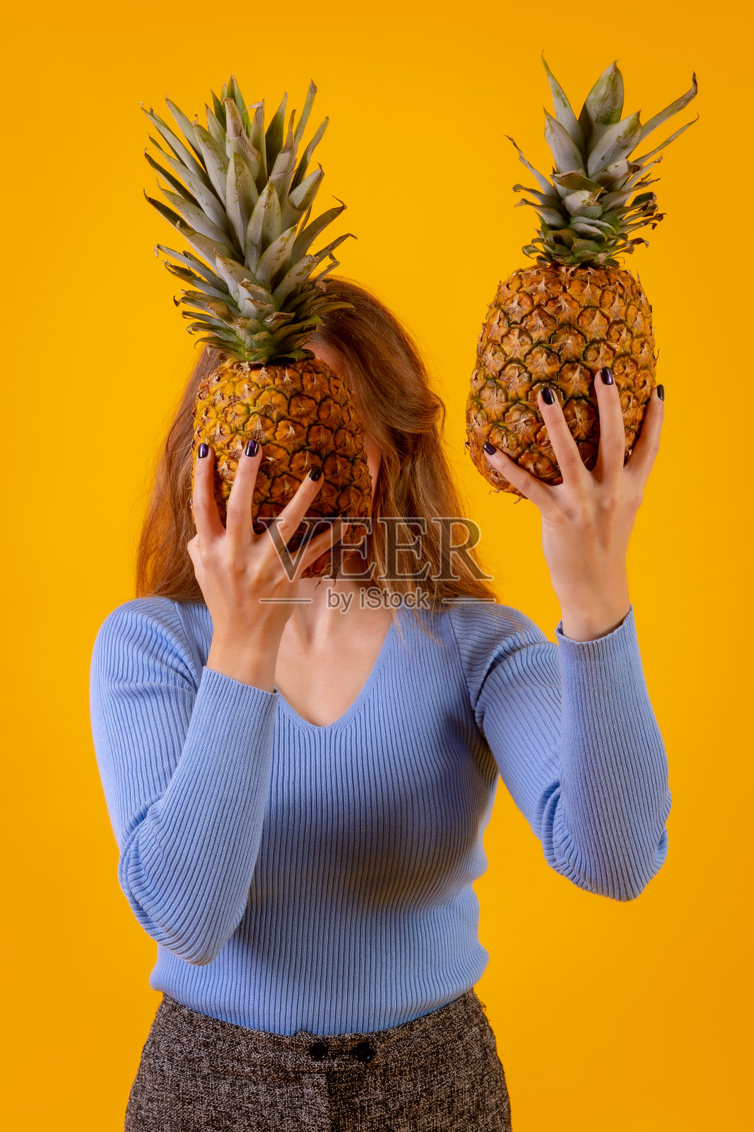 菠萝切成两半，黄色背景，后面一个女人拿着它照片摄影图片