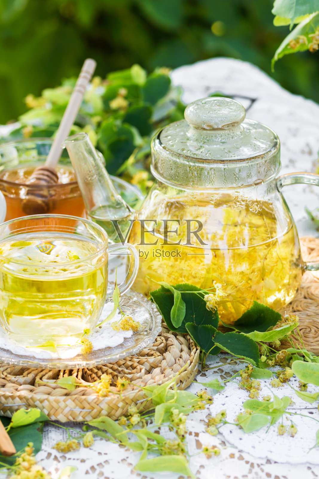 菩提花茶在一个玻璃杯和茶壶上的白色餐巾户外，黄色喝菩提花与菩提花蜂蜜在自然背景照片摄影图片