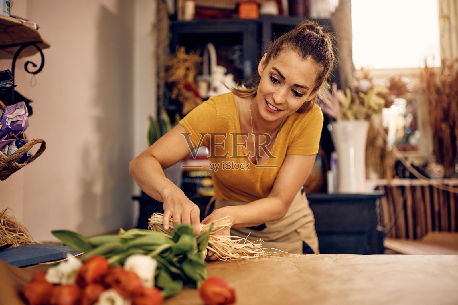 快乐的女花匠安排郁金香在花店的花束。照片摄影图片