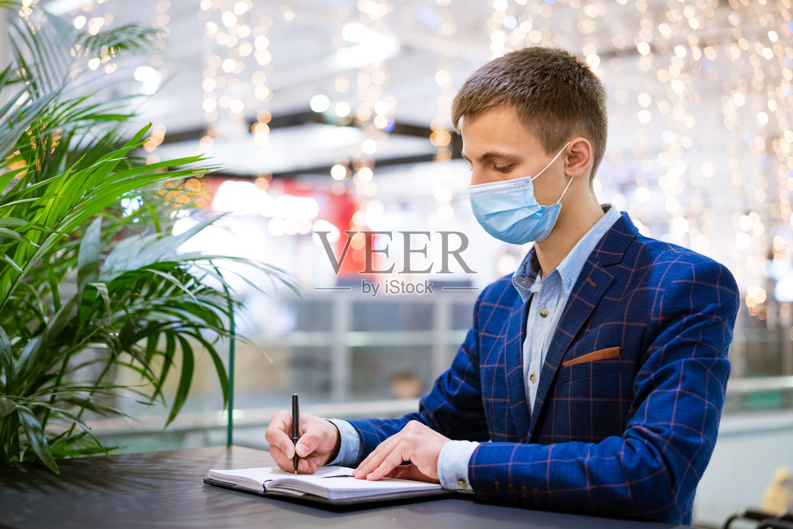 一个戴面具的年轻人在商场里写笔记本照片摄影图片