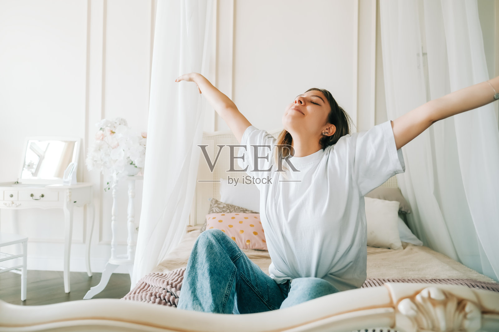 美丽的白人年轻女子坐在床上做伸展运动，享受阳光明媚的早晨。照片摄影图片