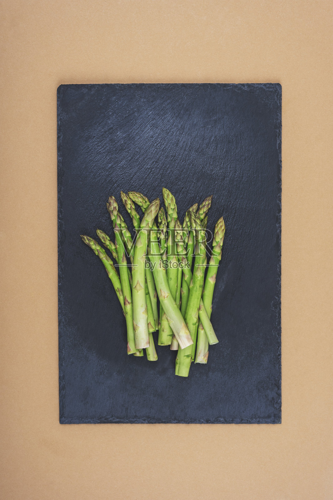 新鲜的绿芦笋放在黑色的石板上，供米色的餐桌食用。健康的素食。俯视图，平铺照片摄影图片