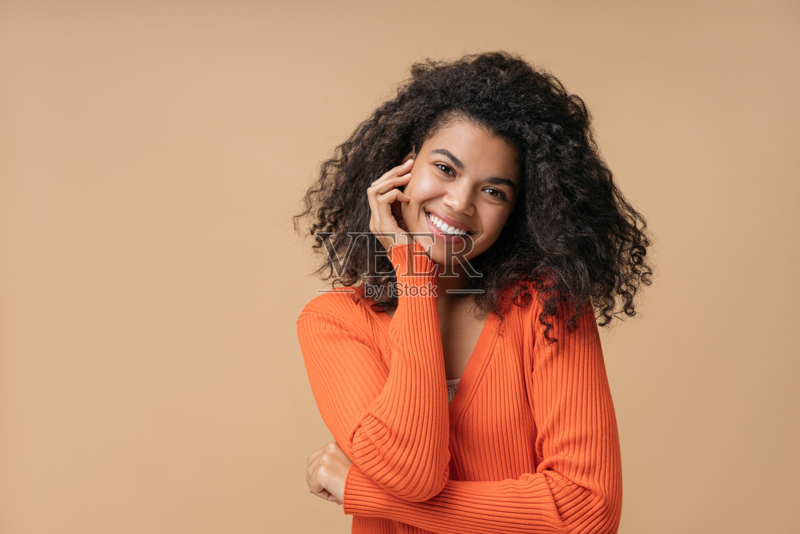 微笑的非洲裔美国妇女与卷发看着相机孤立的背景。年轻自信的时尚模特穿着时尚的橙色毛衣摆姿势拍照照片摄影图片