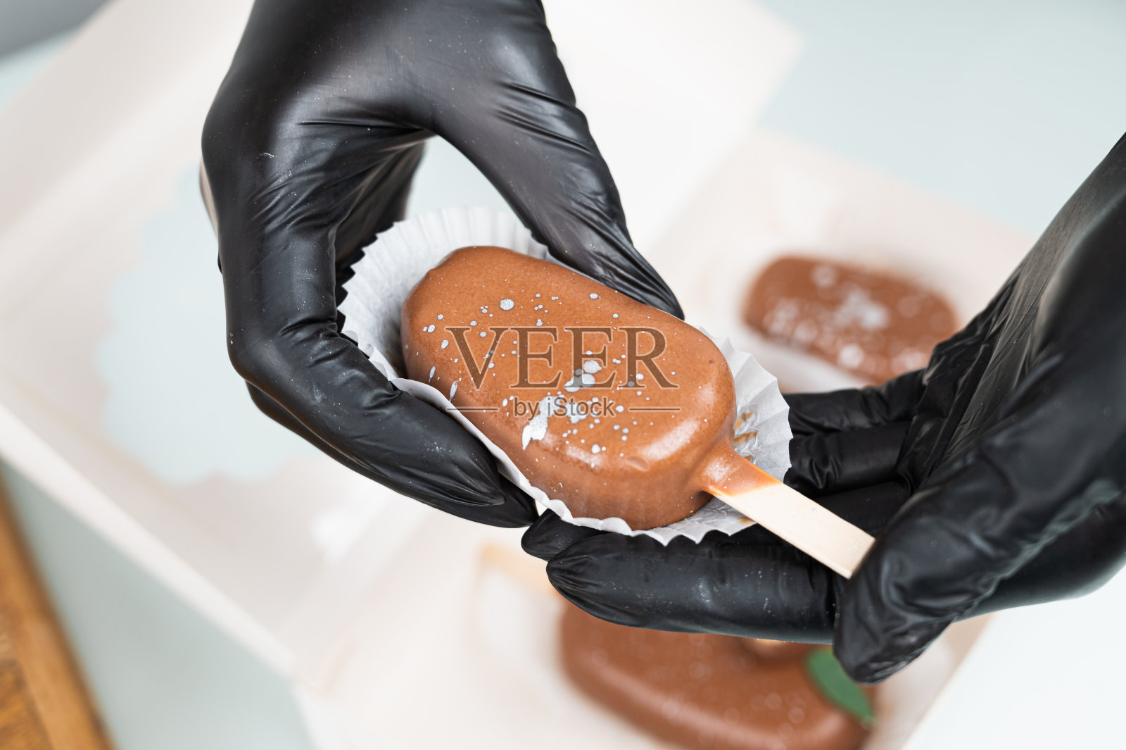 糕点师傅戴着防护手套，把甜点包装在礼品盒里。巧克力蛋糕以冰淇淋的形式出现在棍子上。照片摄影图片