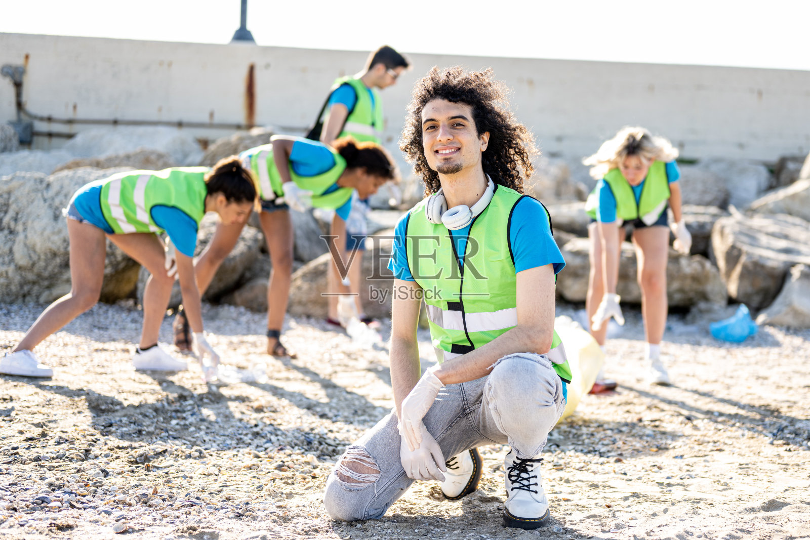 年轻的黑白混血年轻人对着镜头微笑，她的团队在海滩上清理垃圾，志愿者在海岸线上收集垃圾，年轻人意识到海岸线污染照片摄影图片