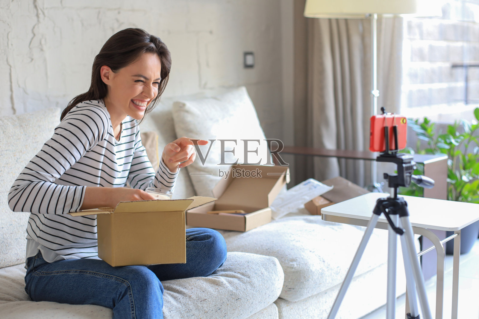 年轻美丽的女博主在家里打开包裹时录制视频。照片摄影图片