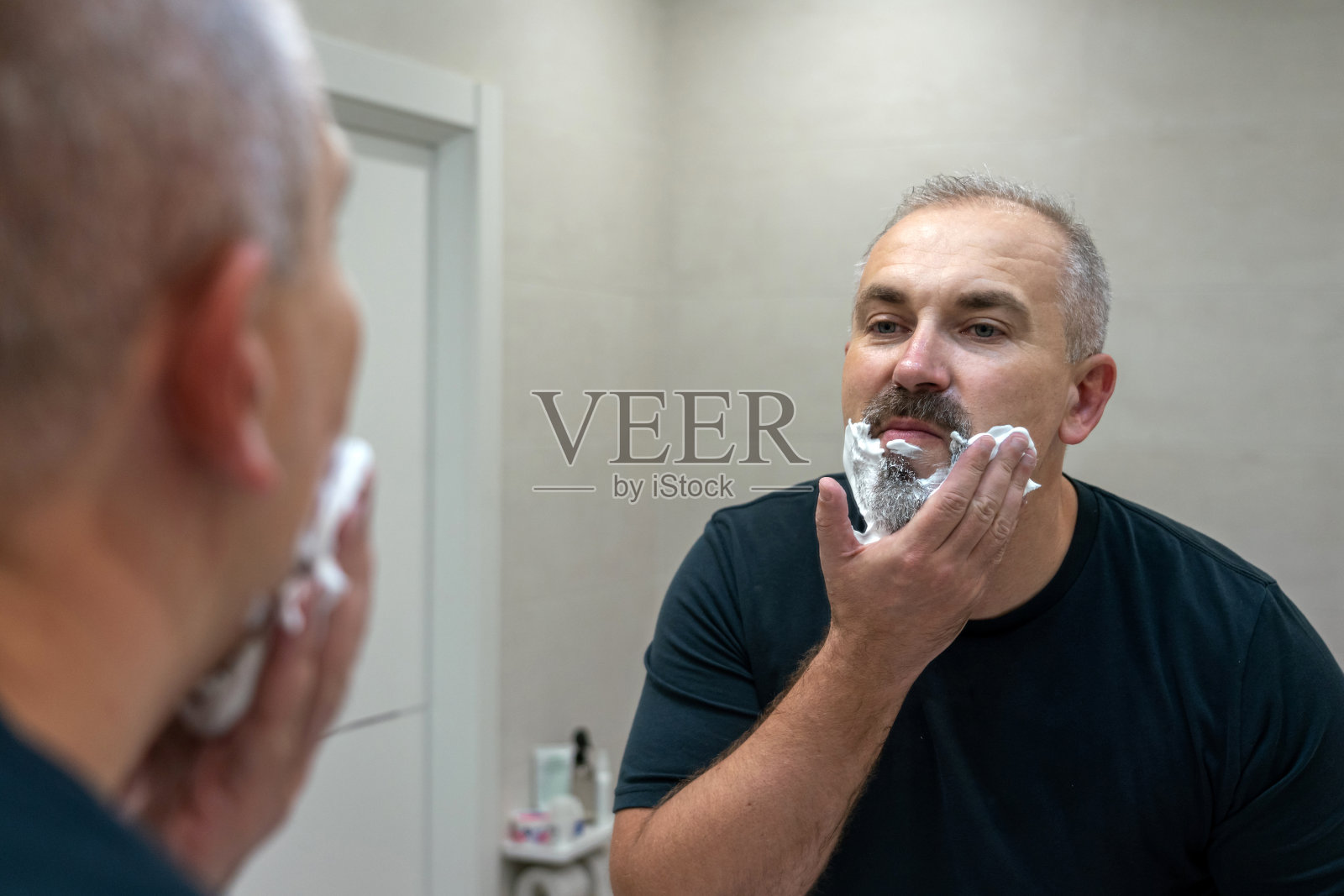 英俊的白发苍老的中年男子正在用剃须泡沫修剪胡子的肖像照片摄影图片