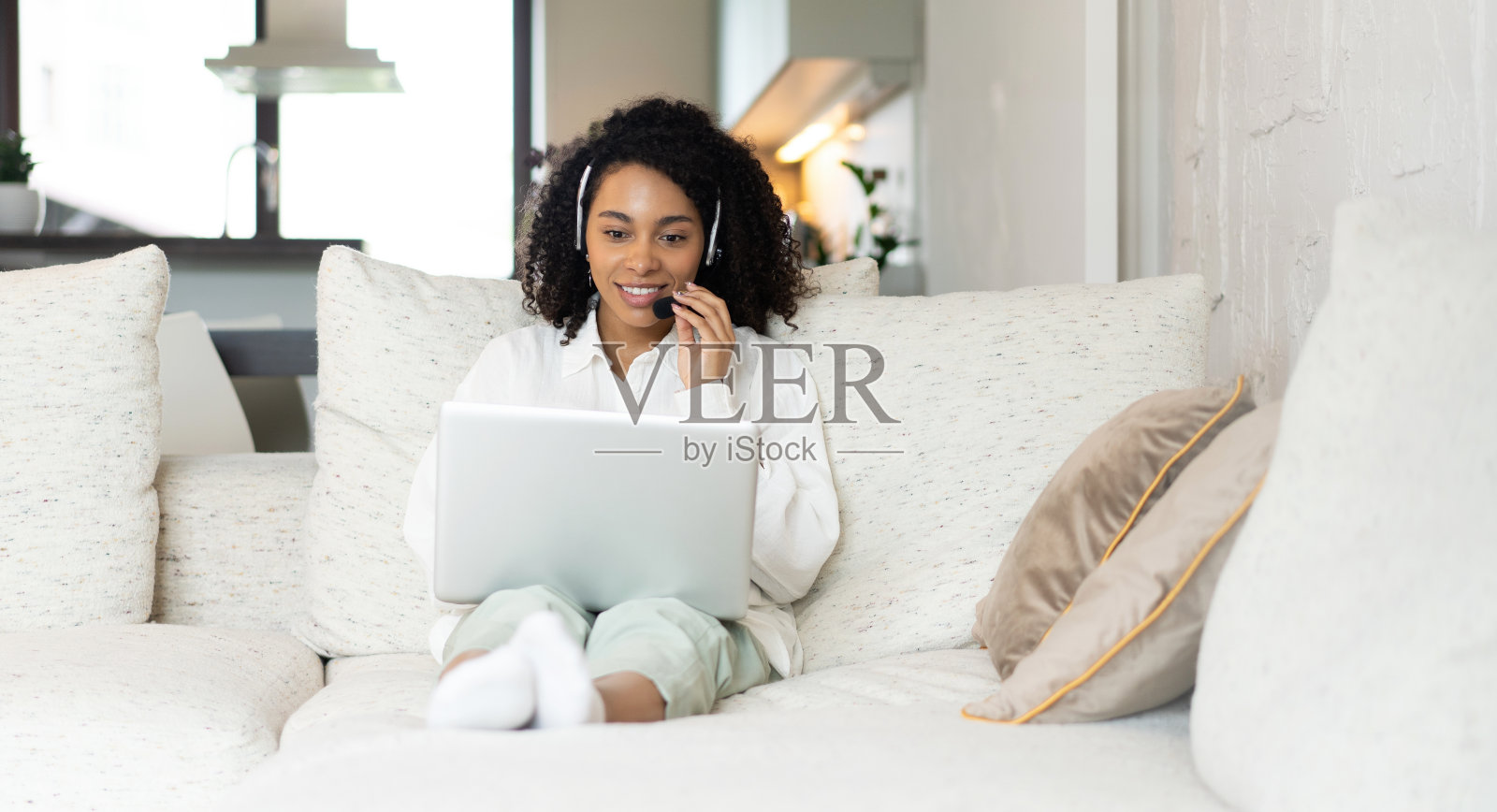 微笑的非洲裔美国妇女戴着耳机使用笔记本电脑，说话，工作的客户支持服务操作员在家里照片摄影图片