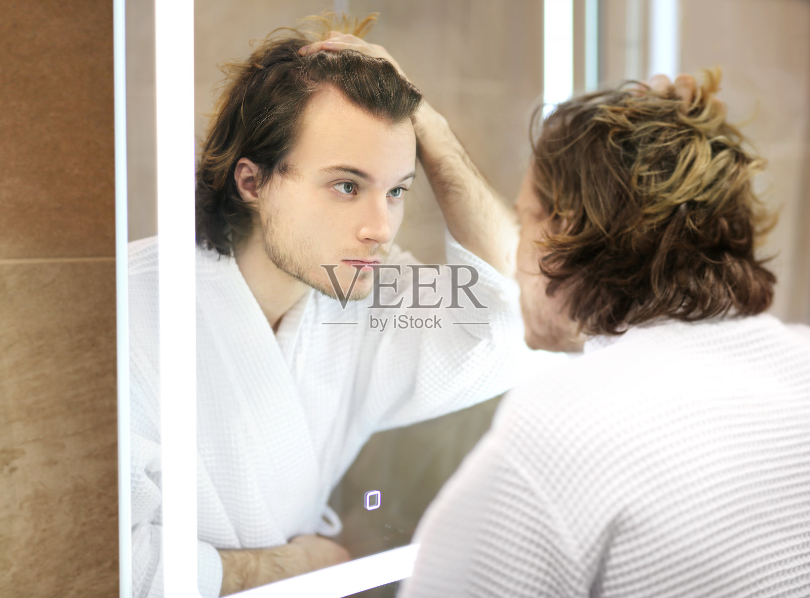 年轻人看着镜子，梳着头发，看着脸上的问题。照片摄影图片