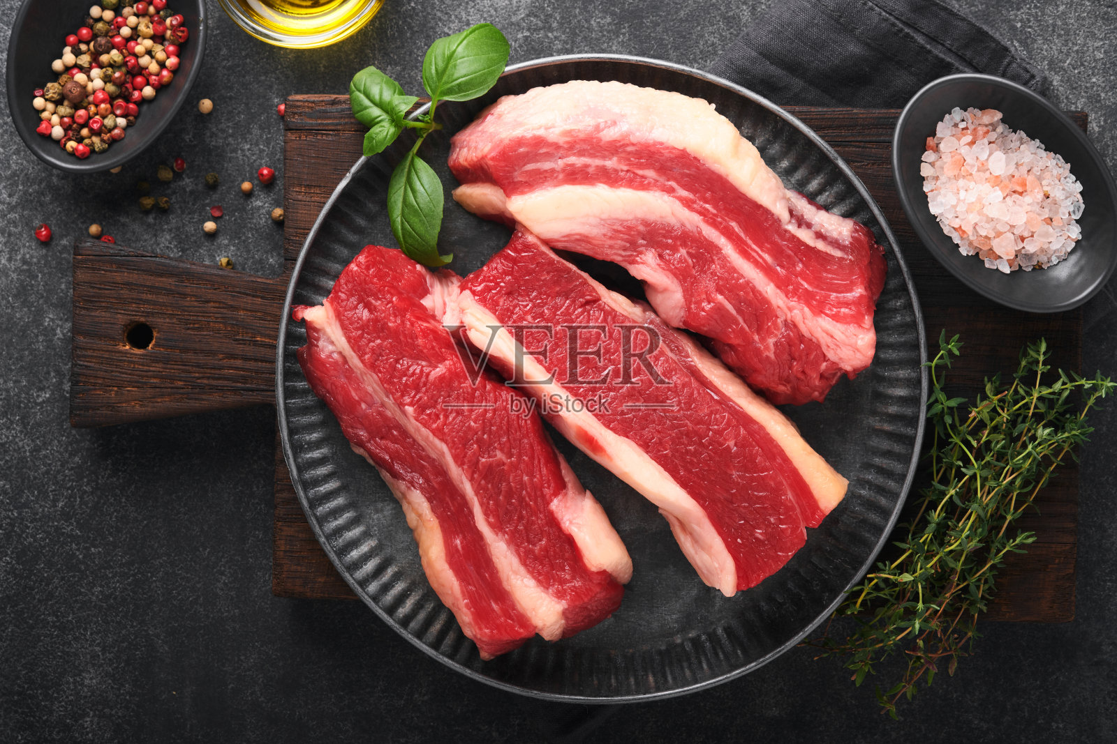 牛排牛肉。纽约生牛排加迷迭香和香料放在古老的铁板上，古老的深色石头背景。前视图。模拟。照片摄影图片