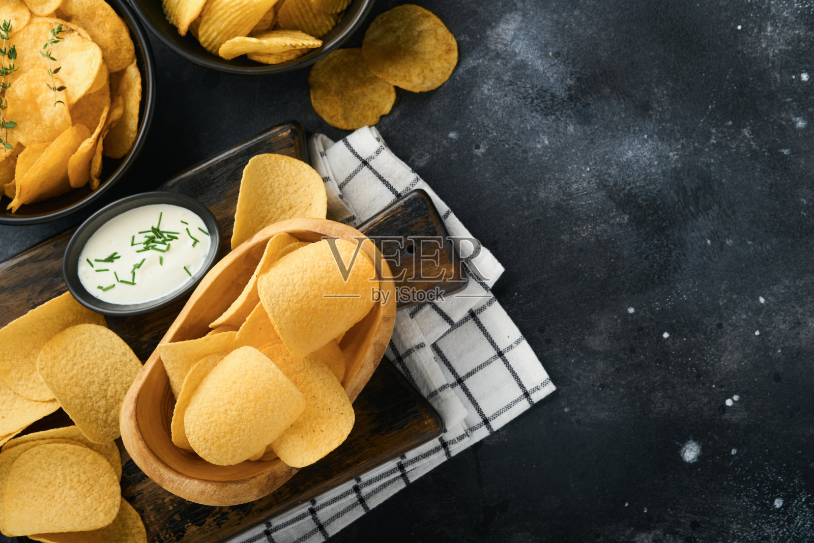 不健康的食物。零食。所有经典的土豆小吃，花生，爆米花，洋葱圈和咸椒盐脆饼，在黑色混凝土背景碗盘。对身材、心脏、皮肤、牙齿都不健康照片摄影图片