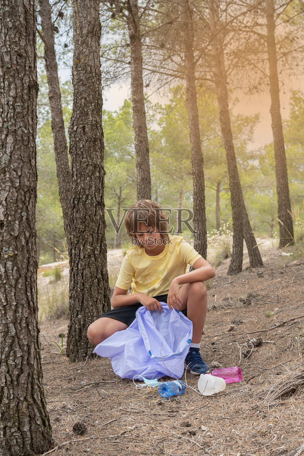 穿黄色T恤的金发男孩在森林里捡拾塑料和瓶子垃圾照片摄影图片