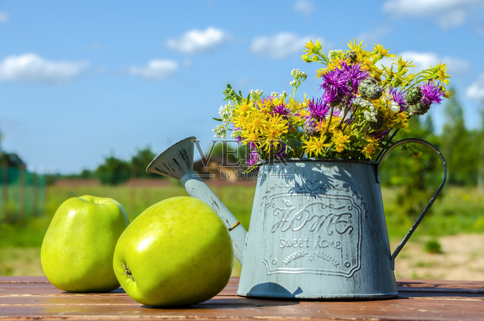 青苹果放在木桌上，还有一个装饰性的喷壶和一束野花。夏天,夏季照片摄影图片
