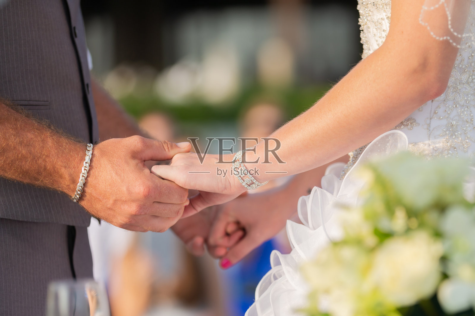 新郎戴着银手镯，新娘戴着钻石手镯，手牵着手。在婚礼上有一道金色的光穿过。照片摄影图片