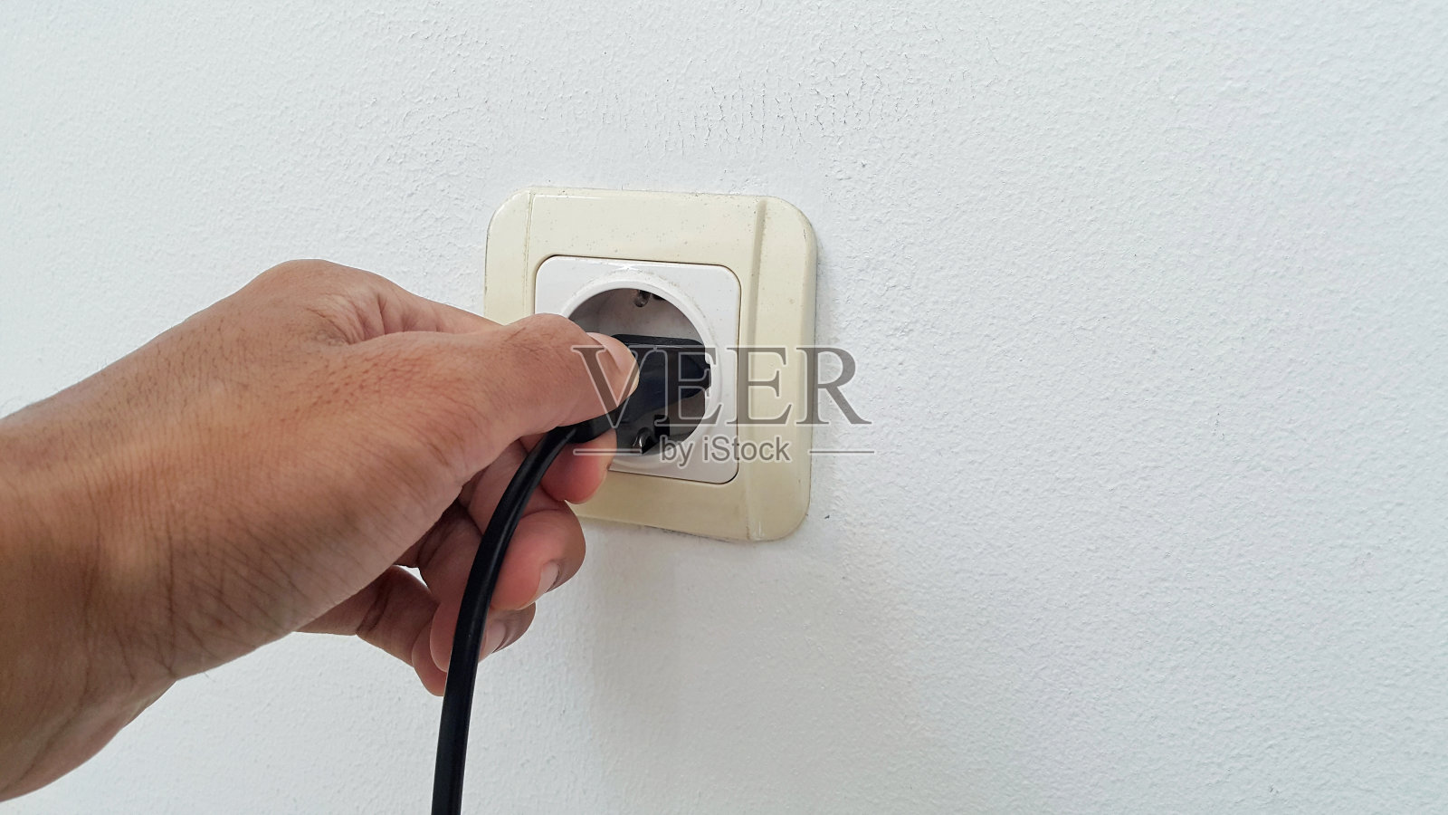 用手把电源线插到白墙上的白色塑料插座上照片摄影图片