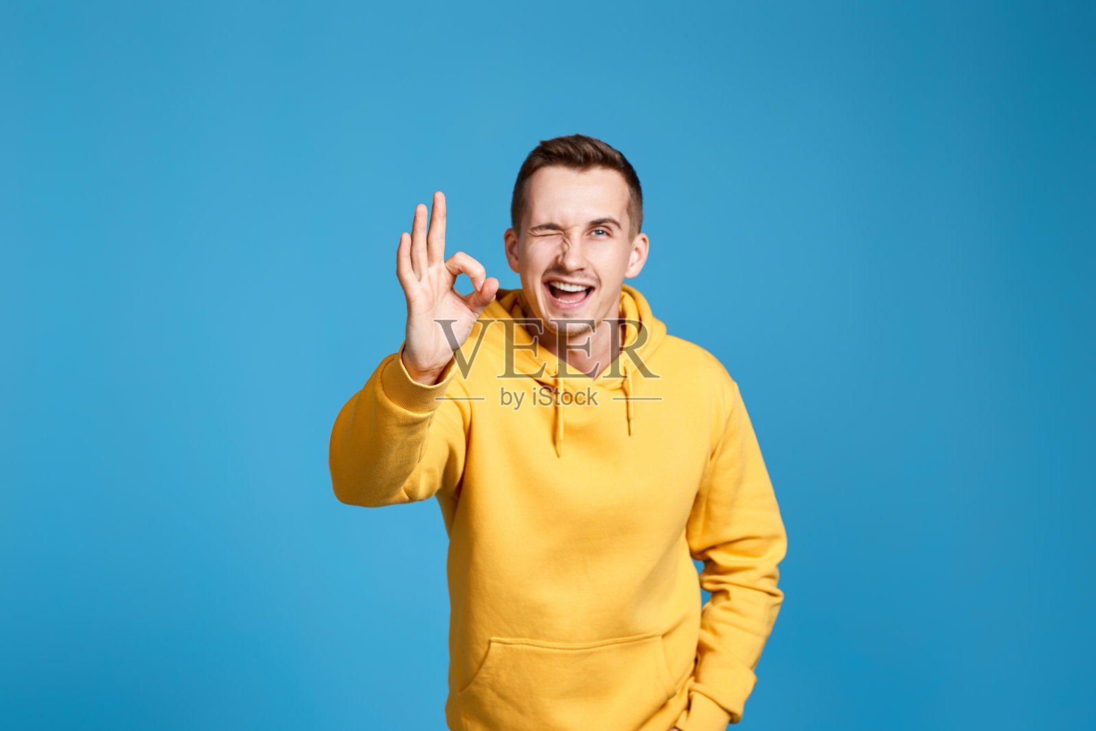 身穿黄色运动衫的年轻人摆出Ok的姿势照片摄影图片