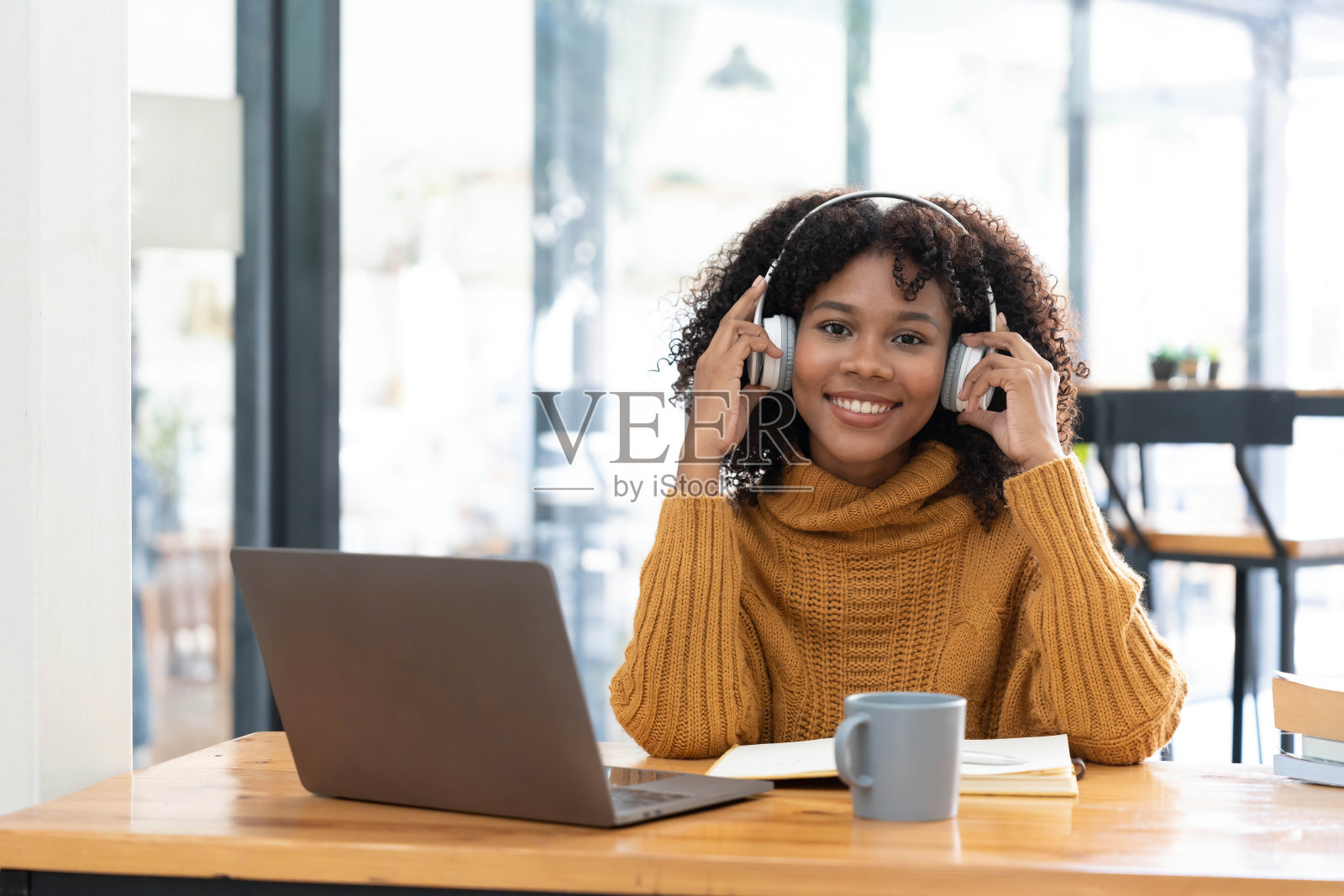 照片的开朗快乐的混血儿妇女在黄色衬衫微笑着工作在笔记本电脑上谈话说话在线视频通话。聪明的少数民族女性戴着耳机在家里的电脑上远程学习。教育的概念。照片摄影图片