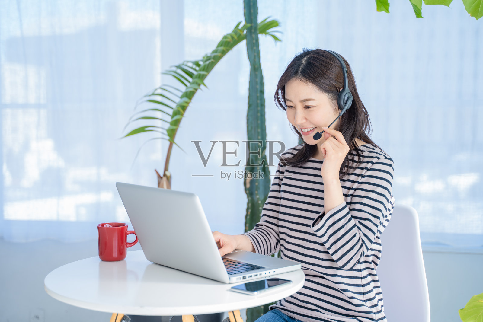 一个戴着耳机在家工作的女人。照片摄影图片