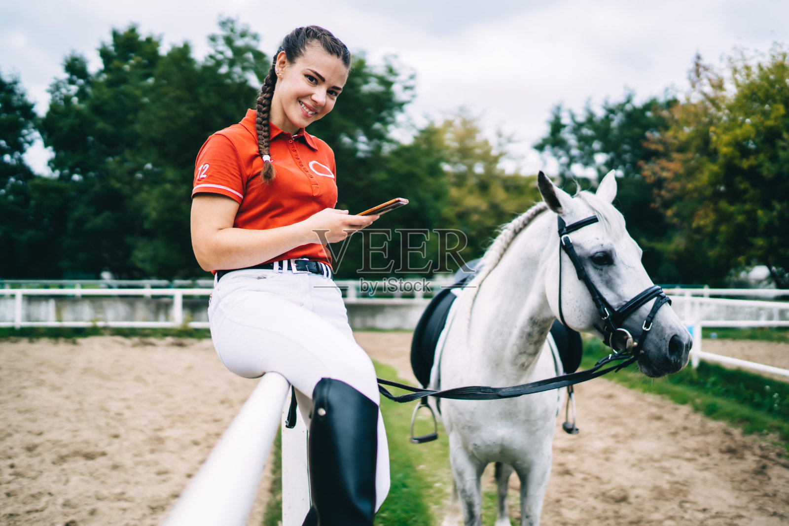 白人女骑师在盛装马术训练后休息的肖像，种马冠军手持现代智能手机，对着相机微笑，快乐的女人用手机度过周末的爱好照片摄影图片