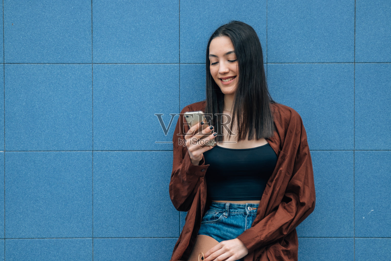 年轻女孩拿着手机在街上的墙上照片摄影图片