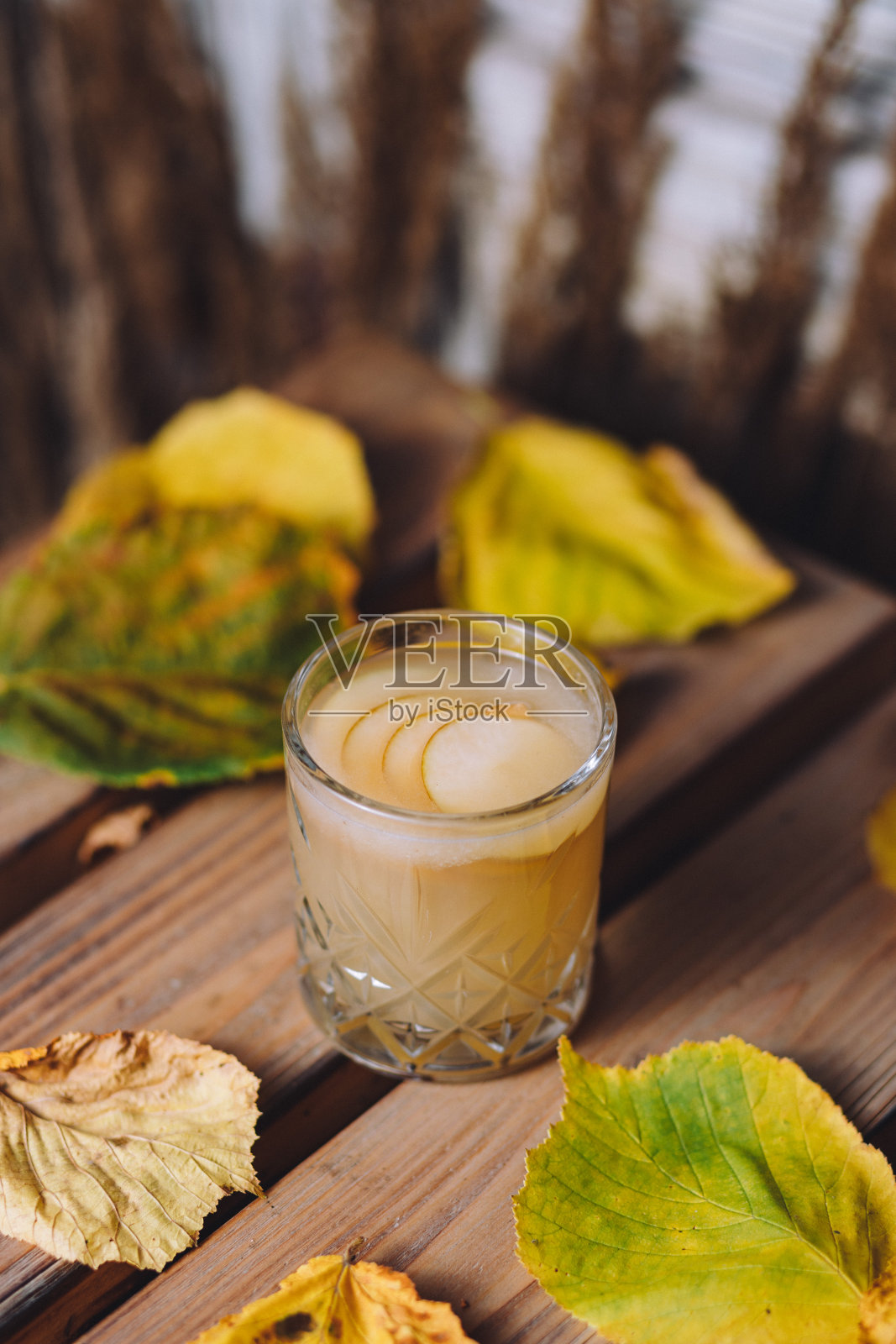 垂直镜头的一杯热热的梨汁在桌子上覆盖着干树叶照片摄影图片