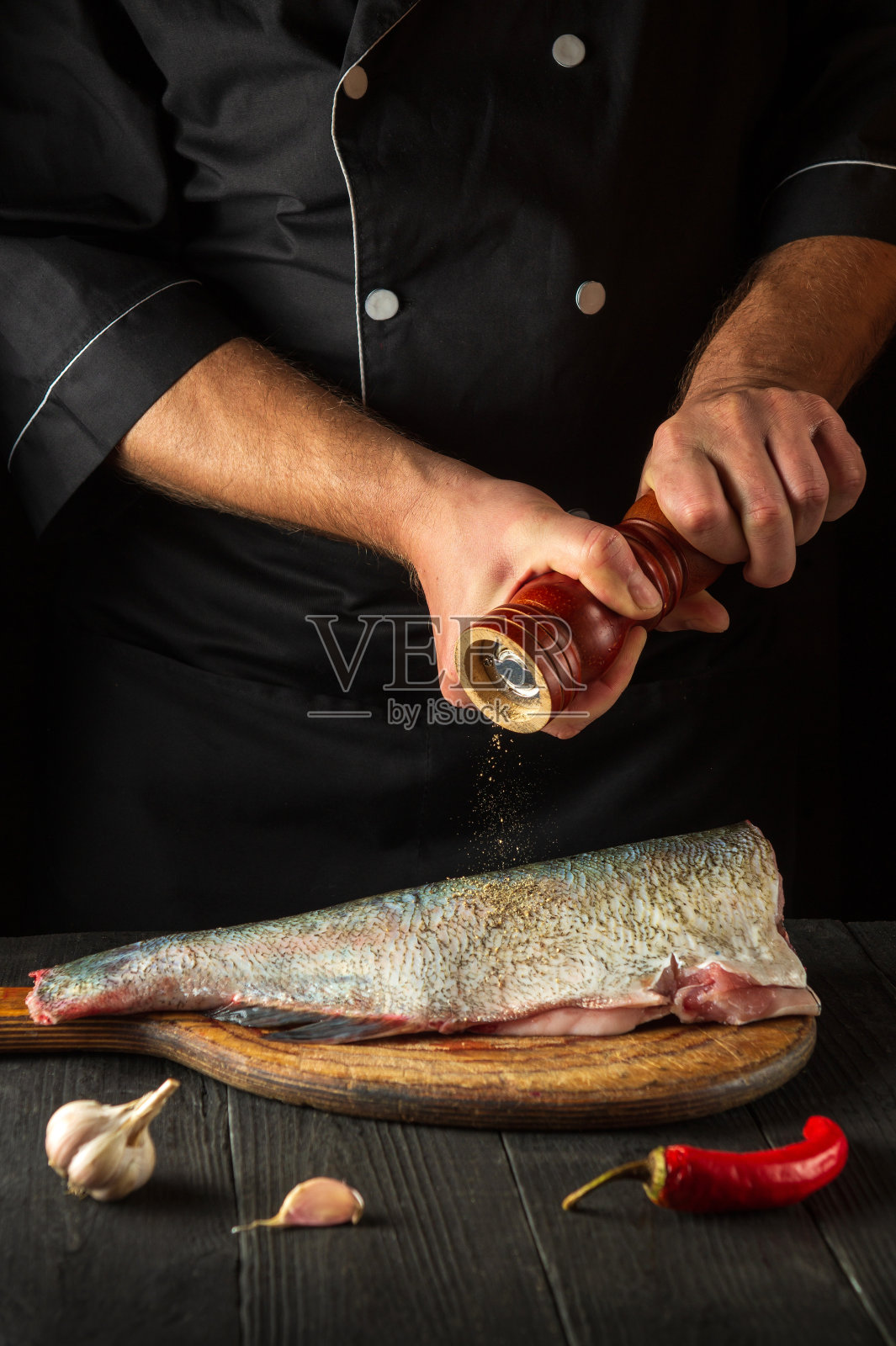 专业厨师准备鲜鱼撒胡椒。准备做鱼食。餐厅或咖啡厅厨房的工作环境。照片摄影图片