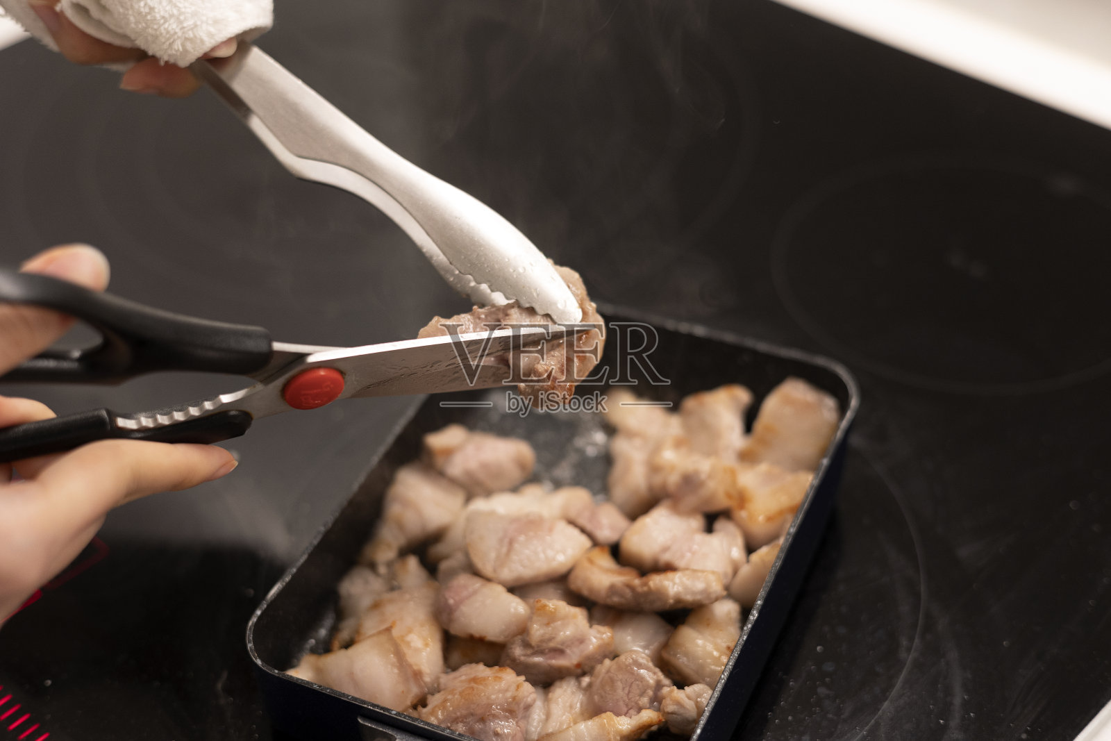用剪刀将肉剪开，用煎锅和火钳将五花肉煮熟照片摄影图片