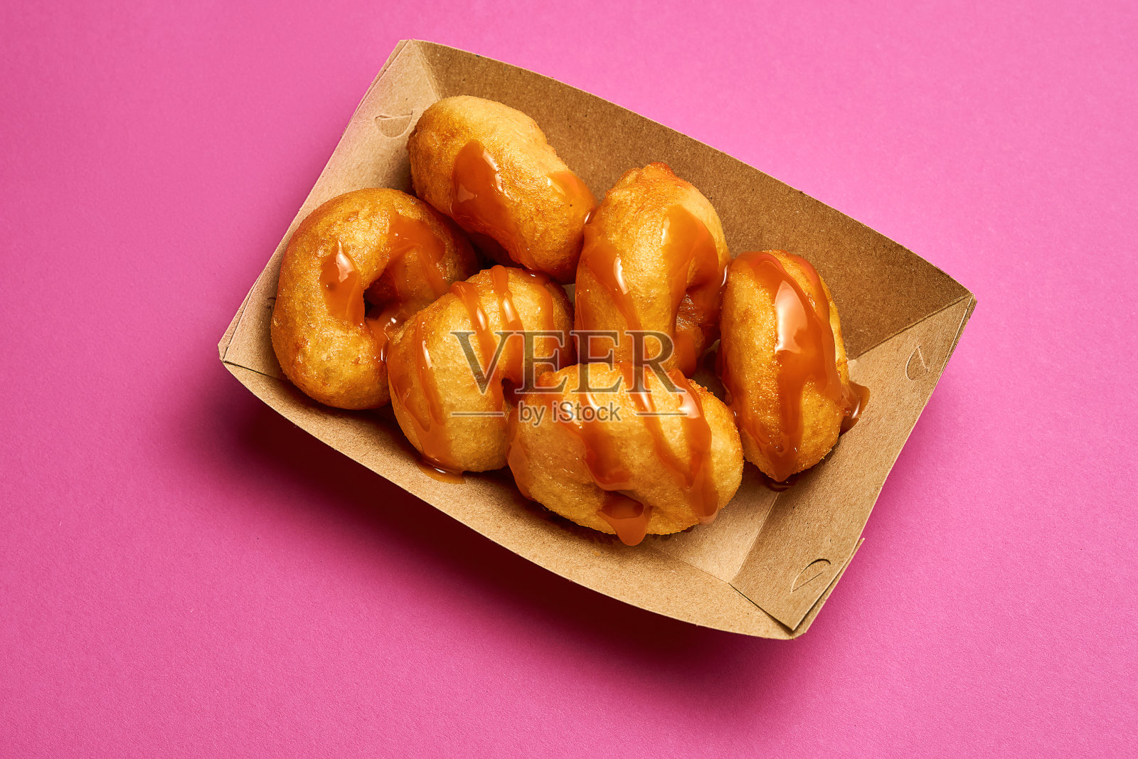 新鲜甜甜圈的顶部视图，粉色背景上撒着焦糖。照片摄影图片