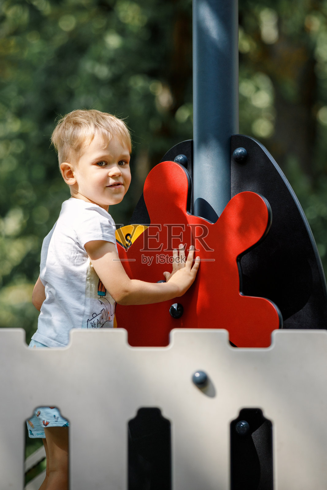 阳光明媚的日子里，男孩像船长或水手一样在船上玩耍。孩子有很多乐趣。船的舵是鲜红色的。照片摄影图片