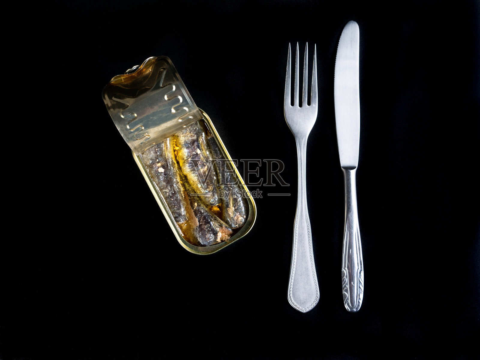橄榄油上的沙丁鱼罐头，刀叉孤立在黑色背景上照片摄影图片