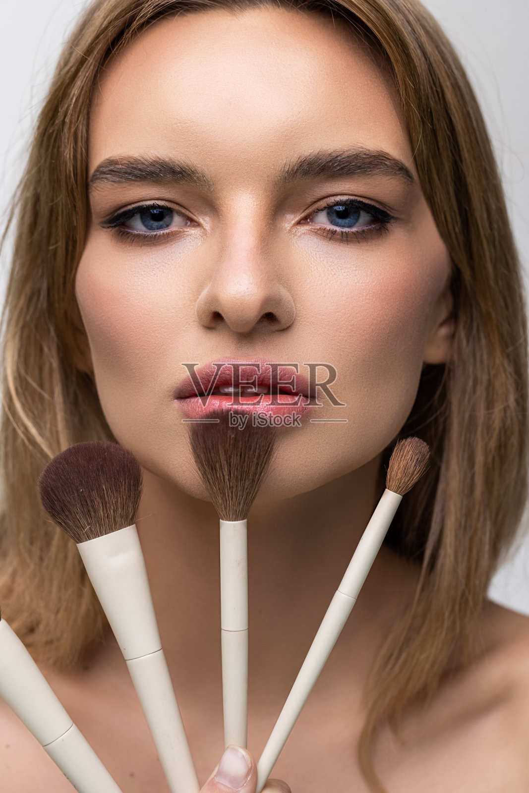 美丽的年轻女子拿着化妆刷接近迷人的脸在白色的背景照片摄影图片