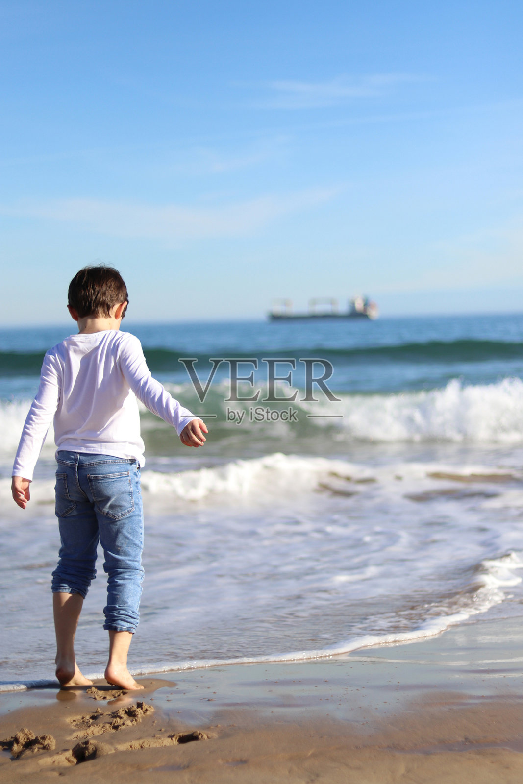 男孩卷起裤腿在沙滩上玩耍照片摄影图片