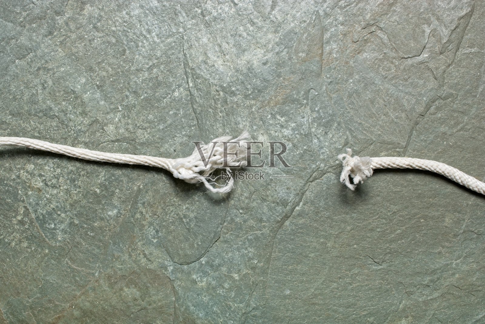 紧张的概念与磨损的两端折断的白色编织绳挂在岩石表面照片摄影图片