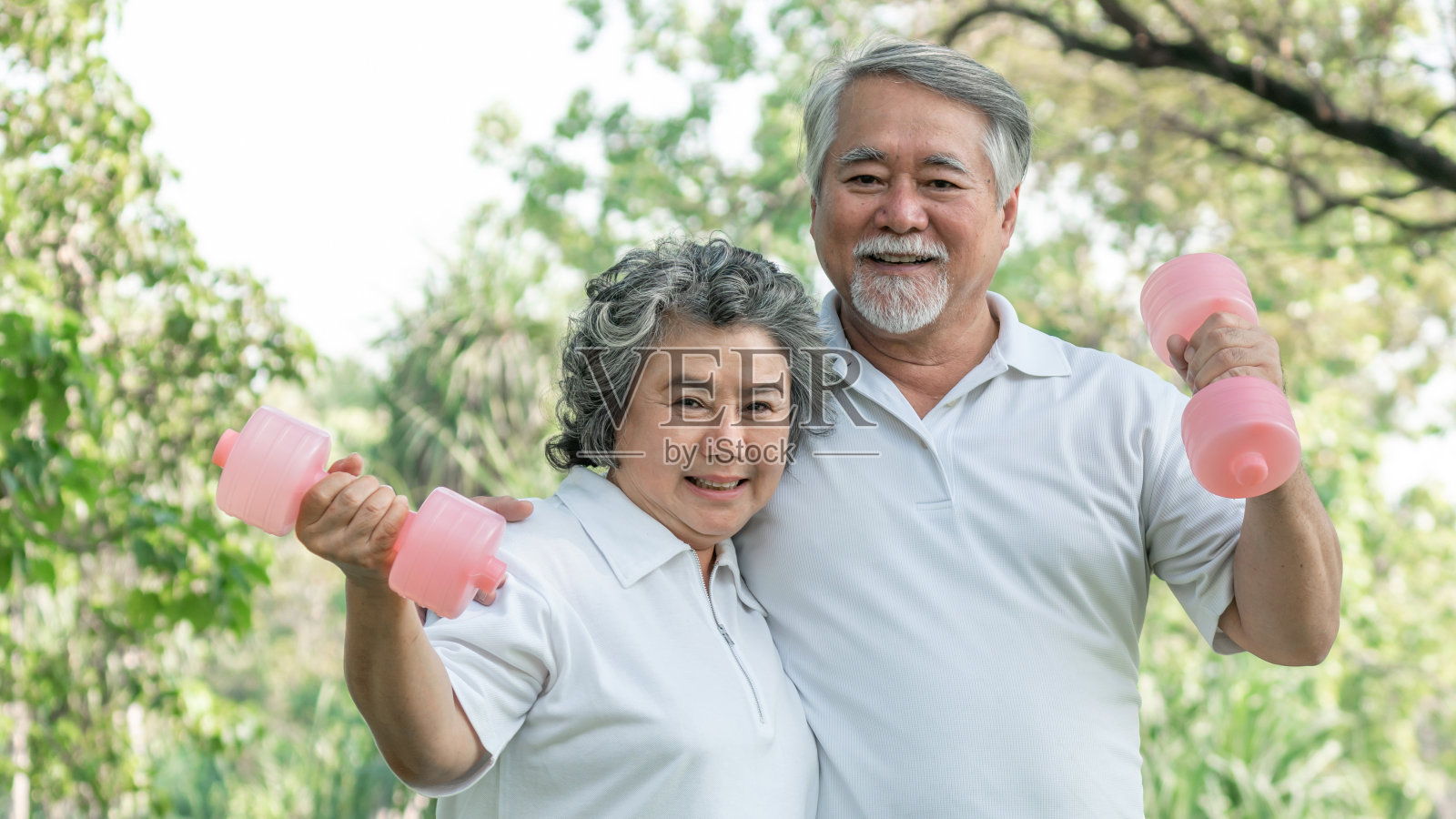快乐的老年夫妇在公园里用哑铃锻炼，他们微笑并拥有健康的身体照片摄影图片