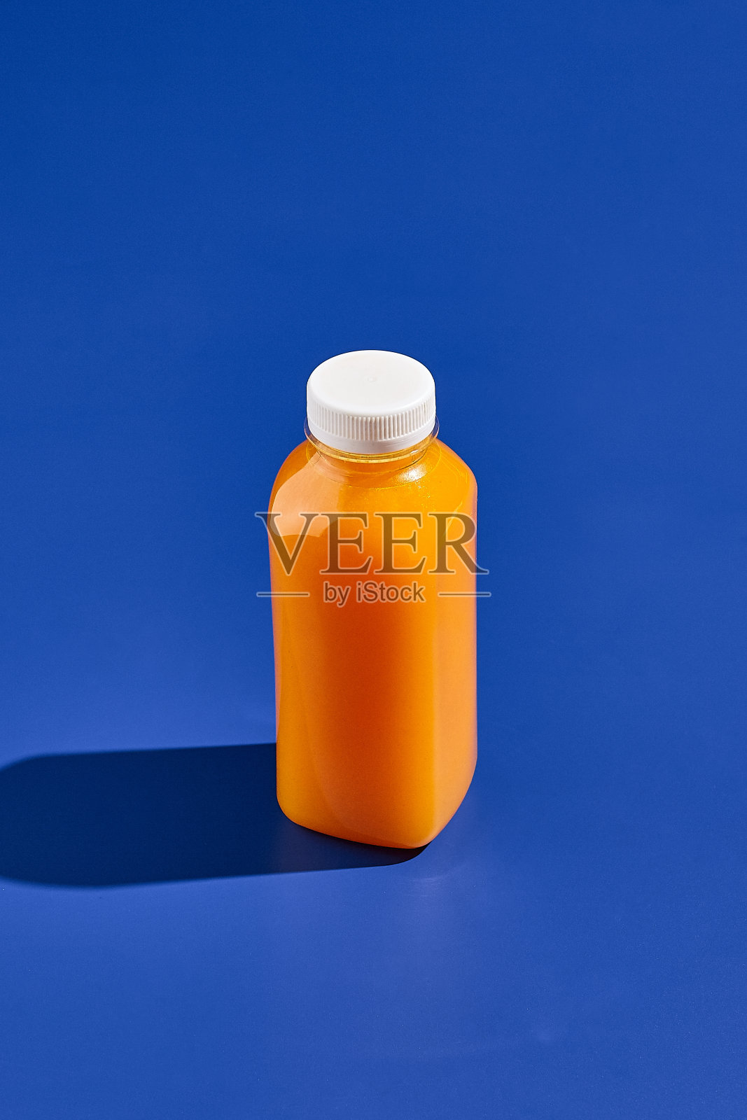 蓝色背景上的橙汁瓶。用塑料瓶喝。交付喝。时髦的模拟瓶概念设计。最小风格的饮料容器。照片摄影图片