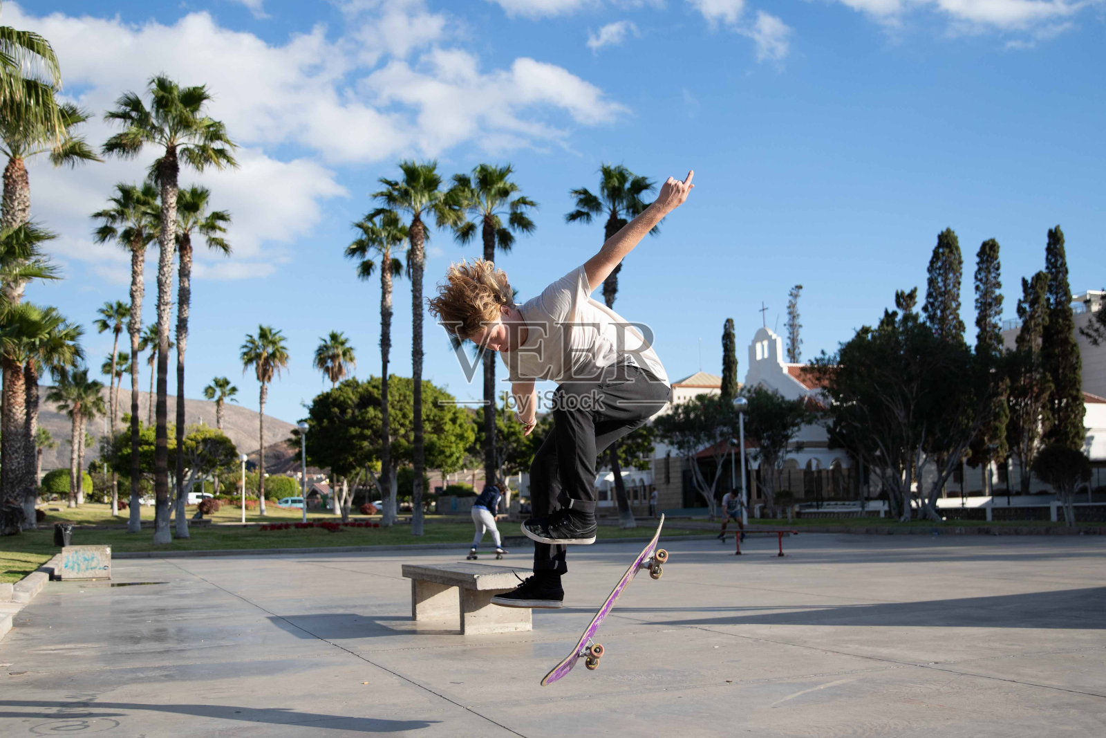 在滑板公园里，滑板者一边玩滑板一边做空翻。照片摄影图片