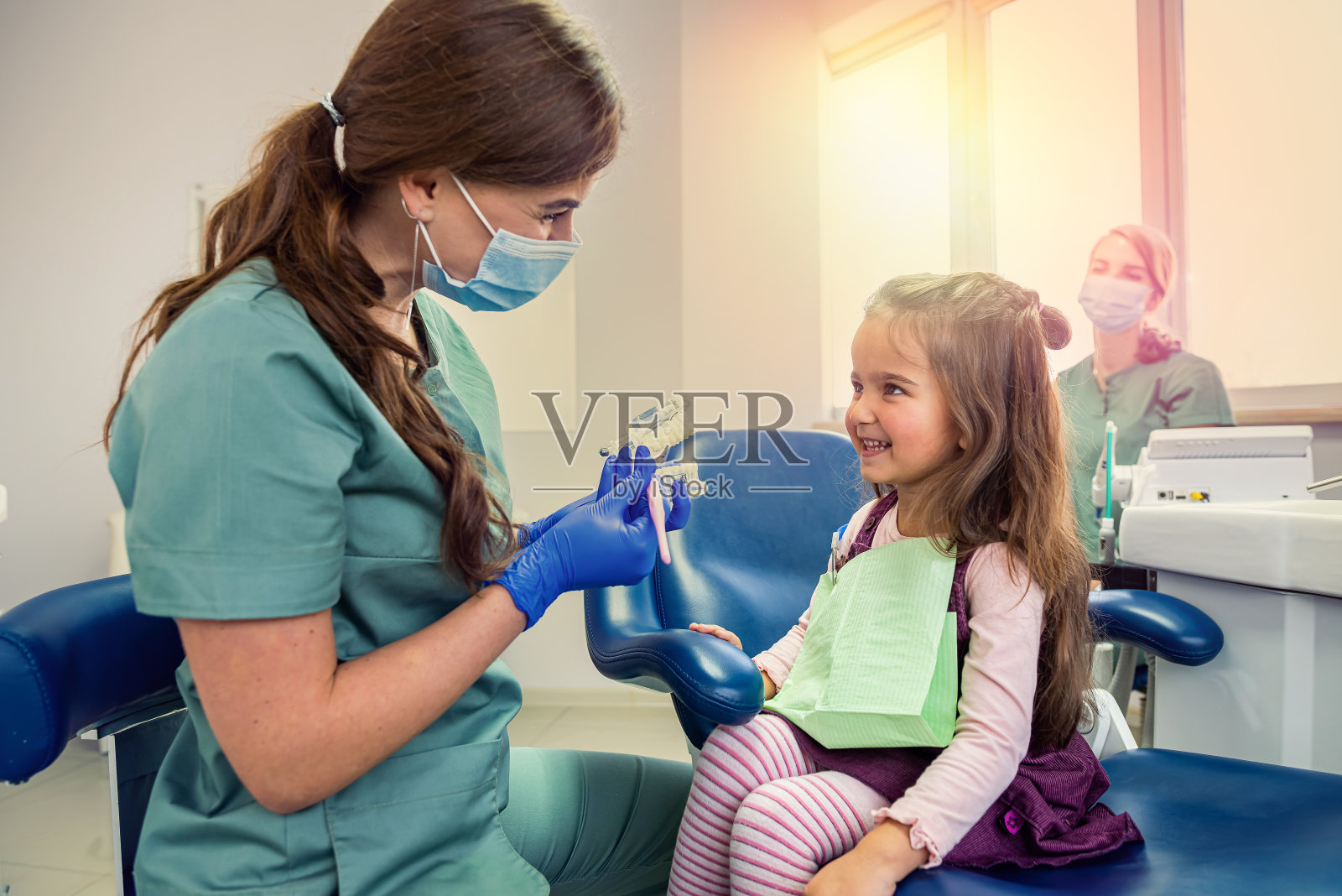 年轻的专业牙医为小客户刷牙，预防龋齿。照片摄影图片