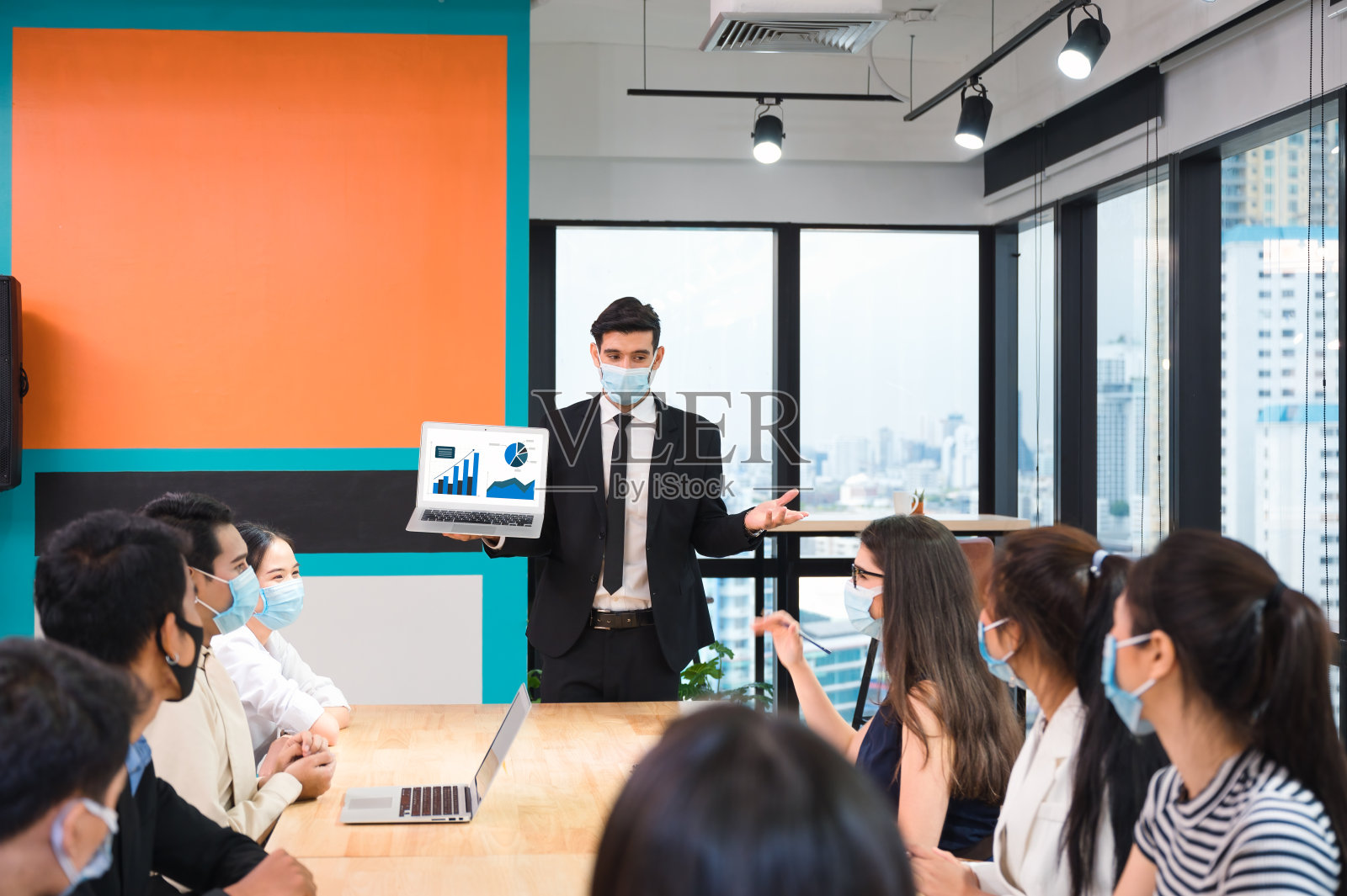 白人商人戴着口罩用笔记本电脑展示商业计划，在新常态办公室与多民族同事进行企业商务会议照片摄影图片