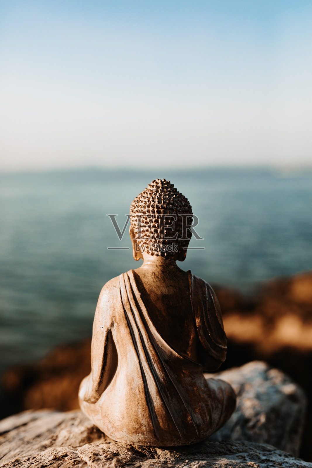 身后的老佛像坐在大海前的一块石头上照片摄影图片