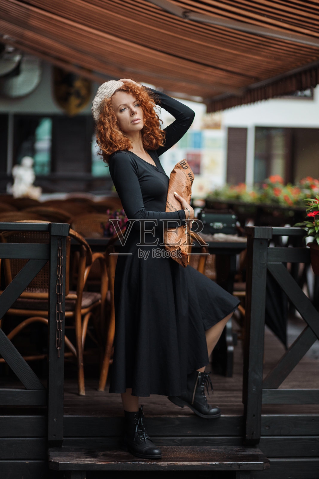 c背景中，一个戴贝雷帽、穿着黑色连衣裙的女人手里拿着一个长棍面包照片摄影图片