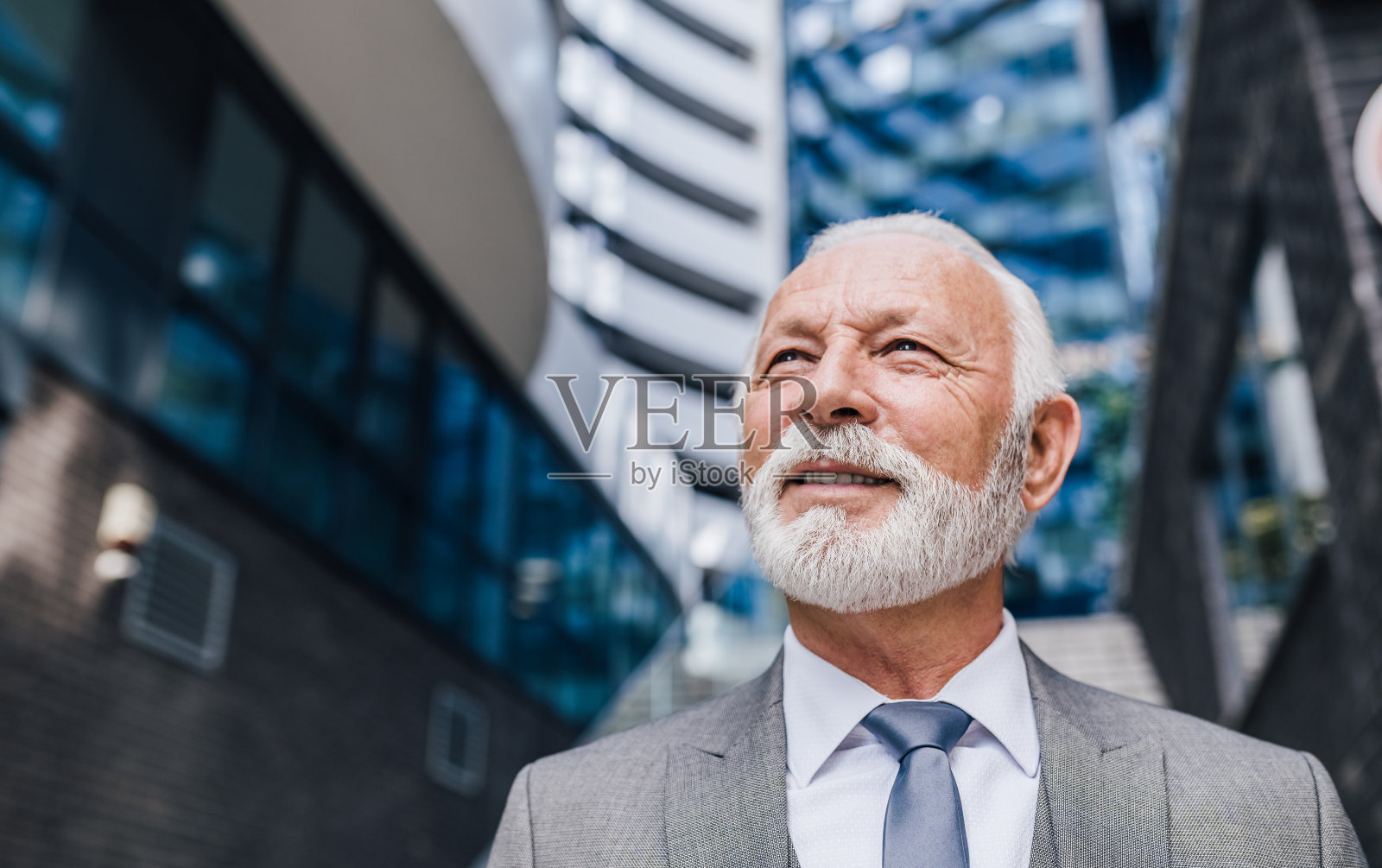 年长的商务人士站在办公大楼外看向别处。照片摄影图片