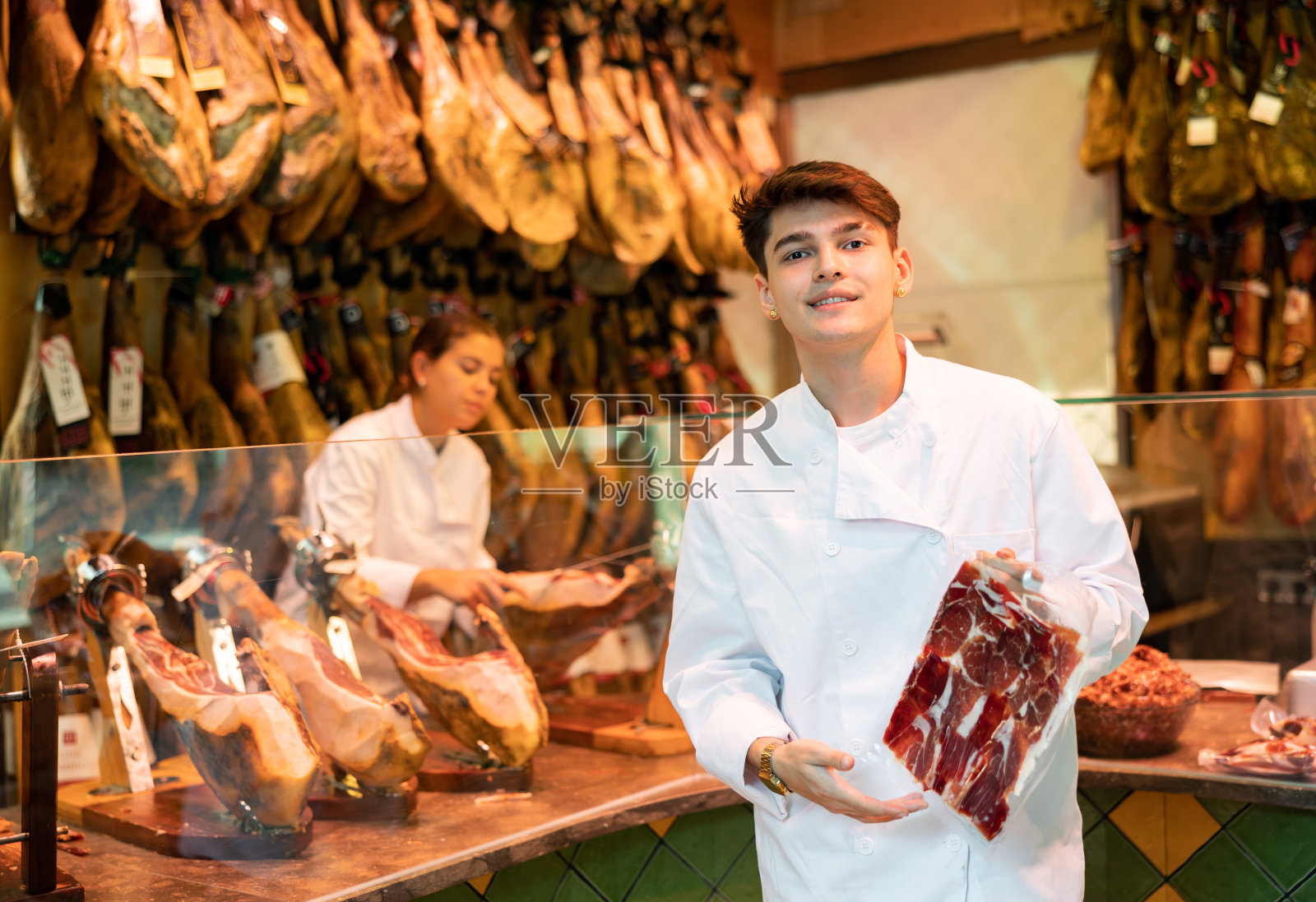 身穿白色制服的年轻肉店卖家提供真空包装的切片照片摄影图片