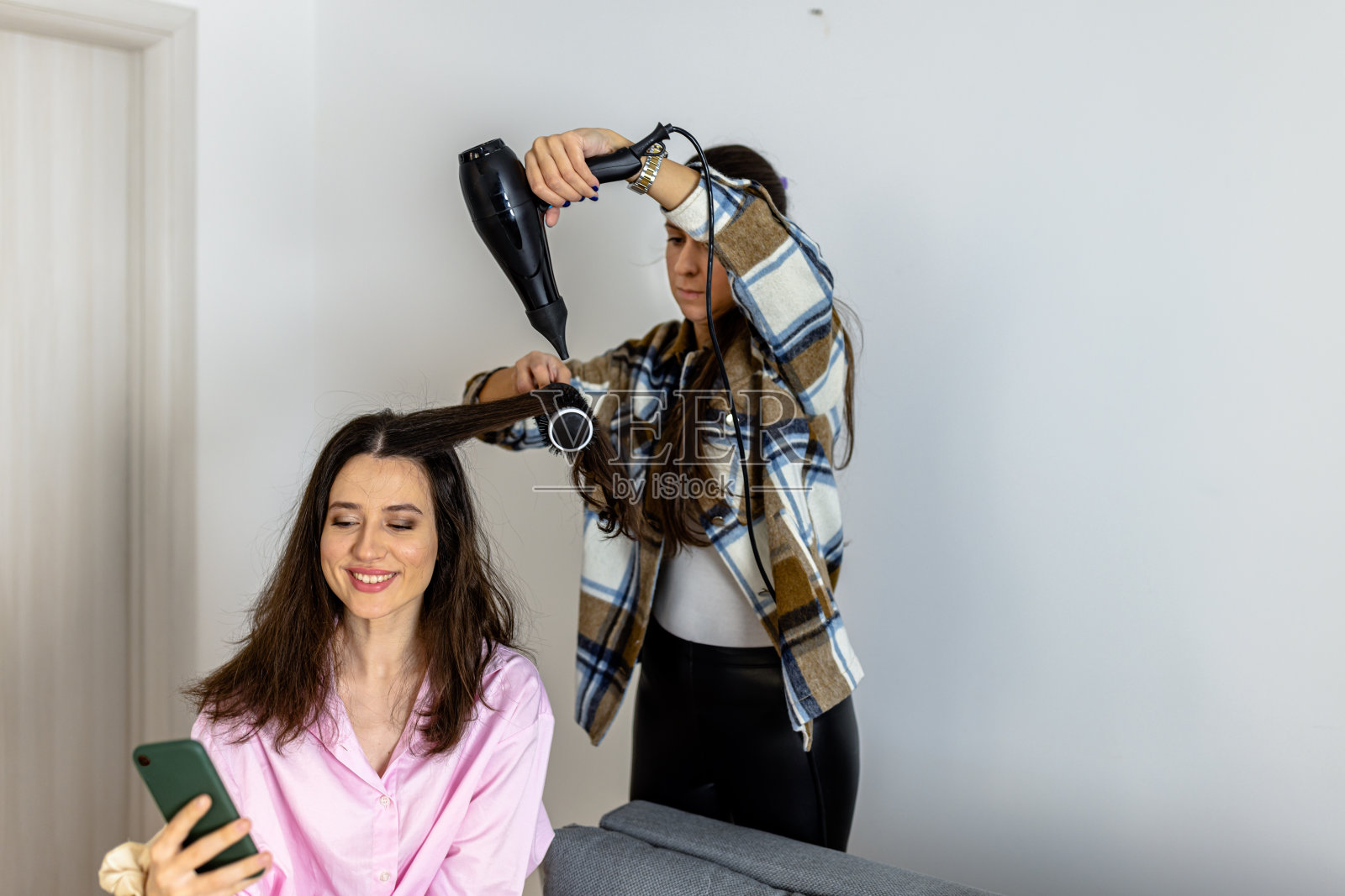 一位职业美发师正在客厅里给一位女士吹头发。照片摄影图片