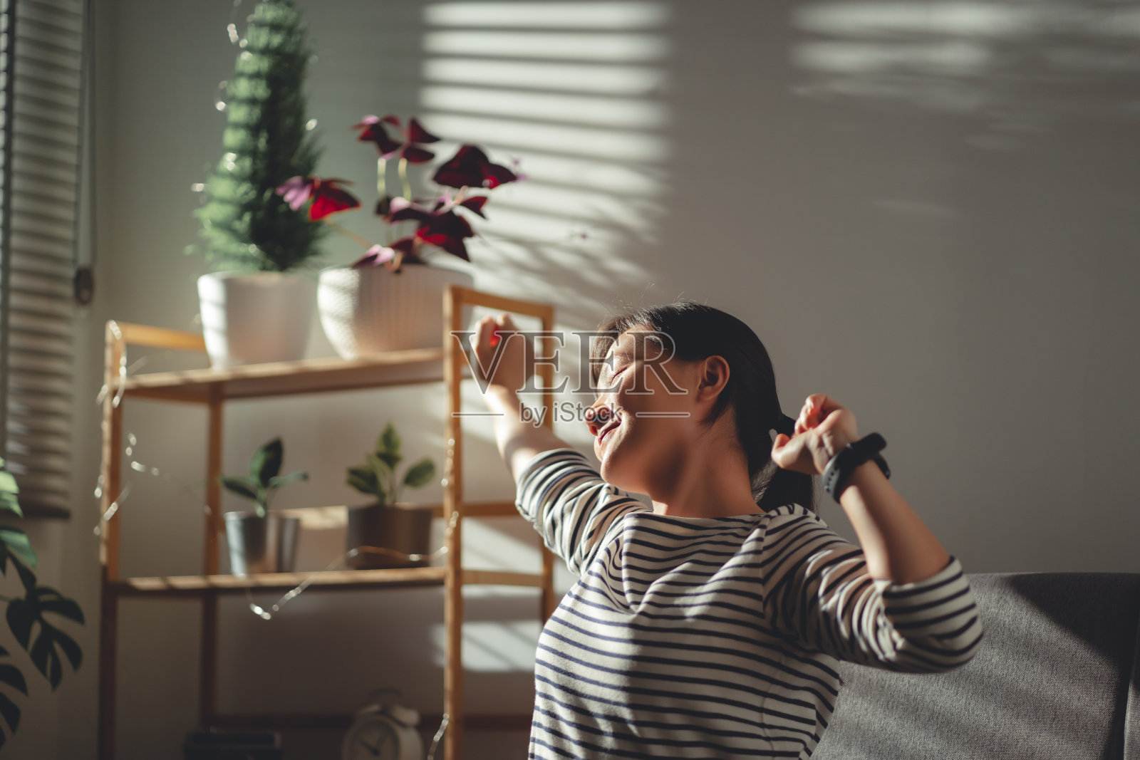 亚洲女人坐在客厅的沙发上放松伸展身体在家里呼吸新鲜空气。照片摄影图片
