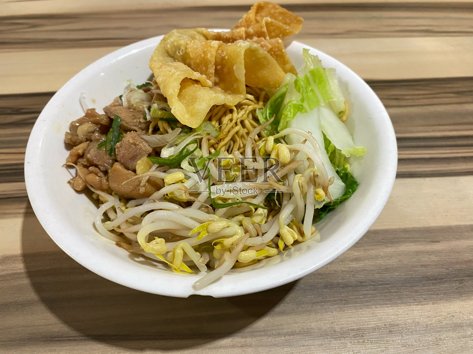 碗三重ayam面条鸡肉与浇头肉和蔬菜与木桌背景或纹理。Mie pangsit ayam照片摄影图片