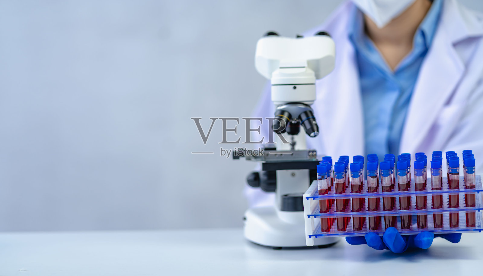 在医院血液学实验室，医生手戴医用手套，拿着装有红色血液的试管进行矢状显微镜检查照片摄影图片